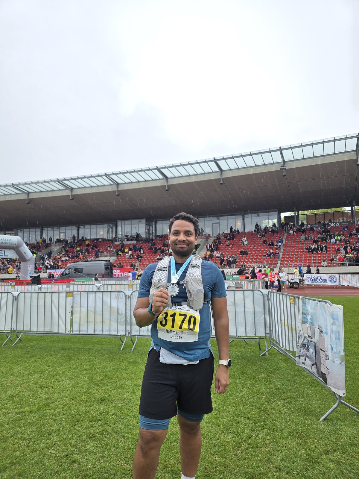 Deepak holding his medal at the stadium after the Kassel Half Marathon 2026, in the rain